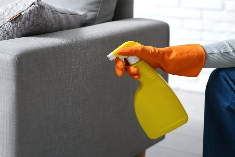 A person spraying a cleaning solution onto a couch